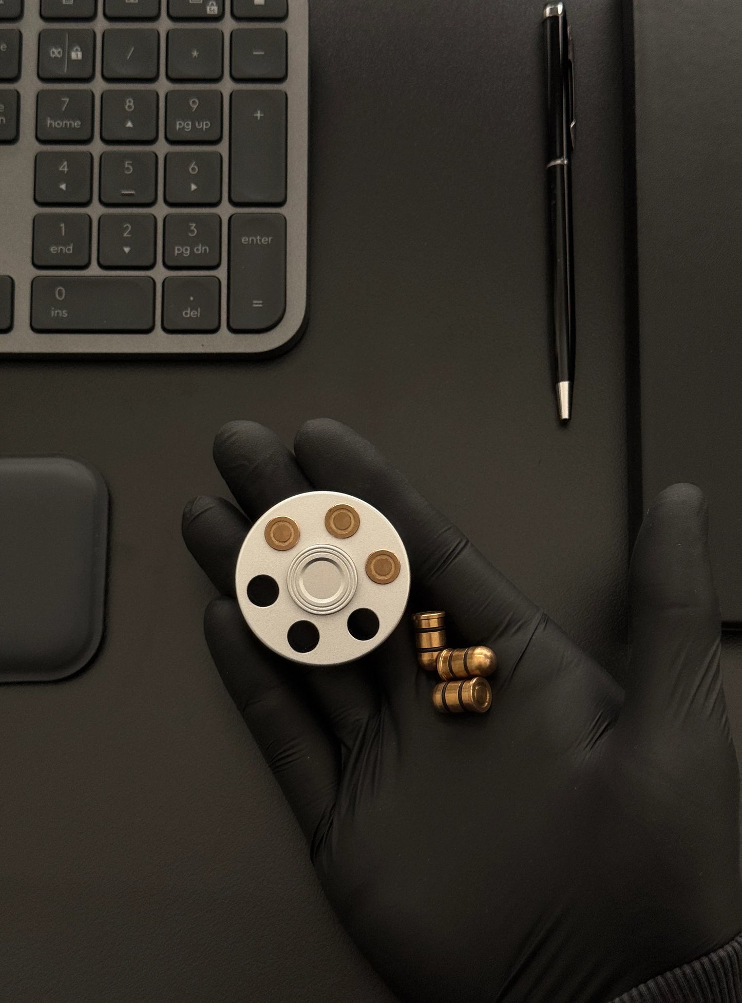 Revolver spinner held in hand next to a keyboard and notebook, emphasizing portability.