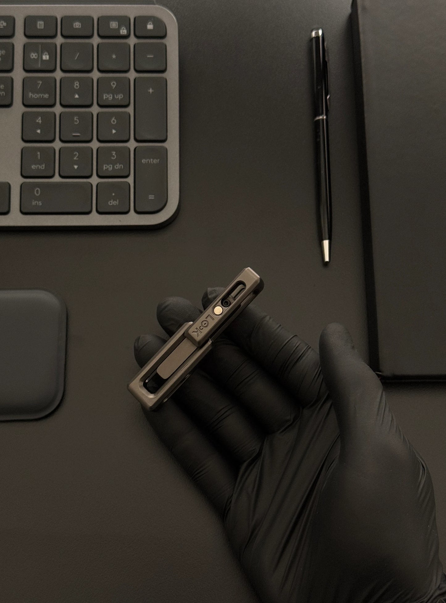 xLock Tower Fidget held in hand on a desk alongside a keyboard and notebook, illustrating its compact size and suitability for workspace use.​