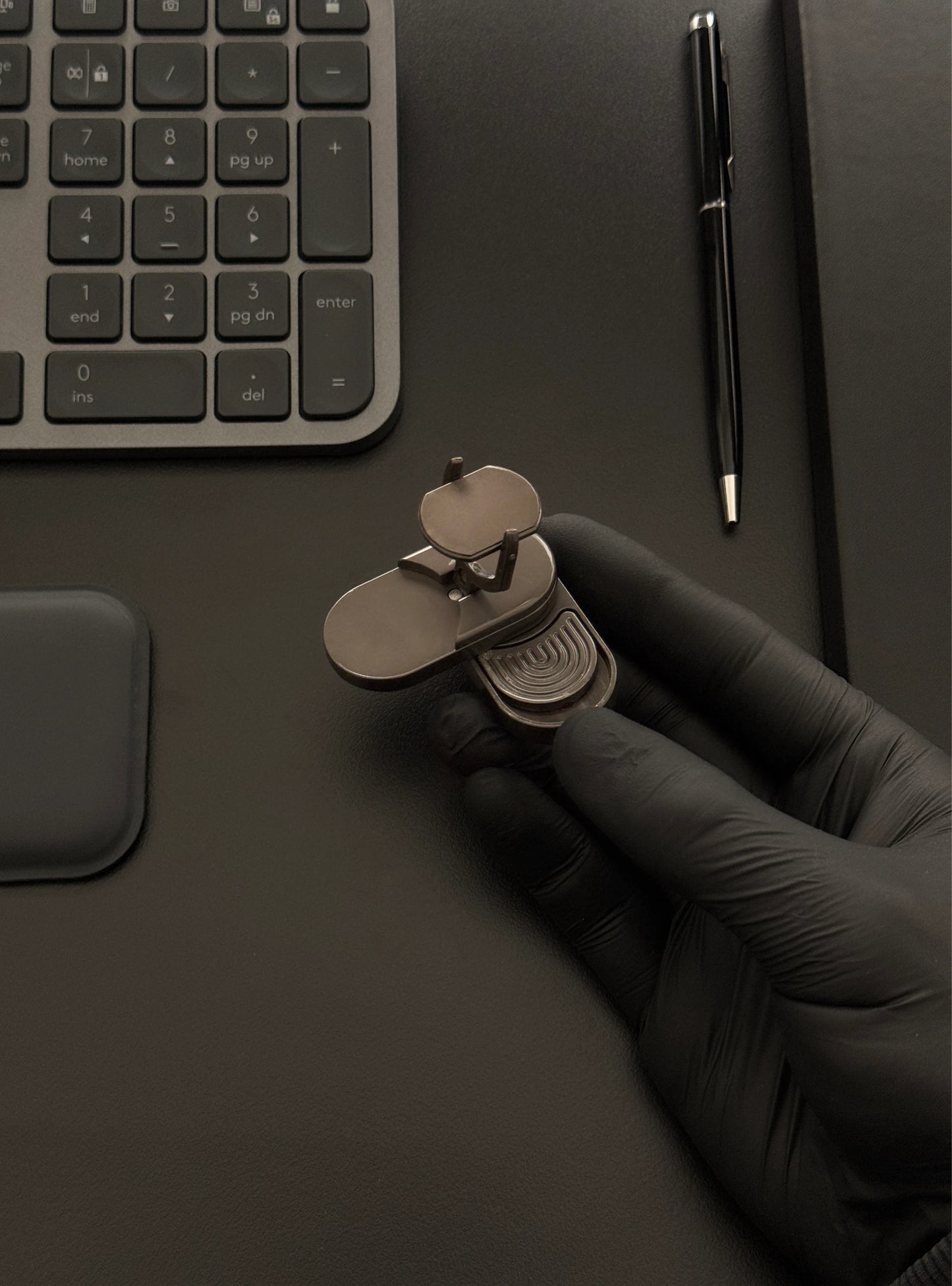 Coin slider fidget toy held in hand on a desk alongside a keyboard and notebook, illustrating its compact size.​
