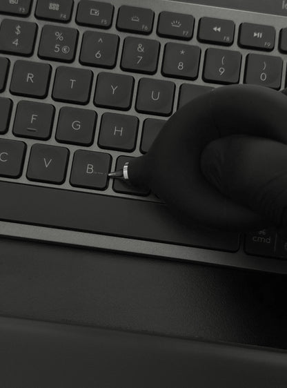 Precision Air Blower held in hand above a desk with a keyboard and notebook, demonstrating practical size and everyday usability