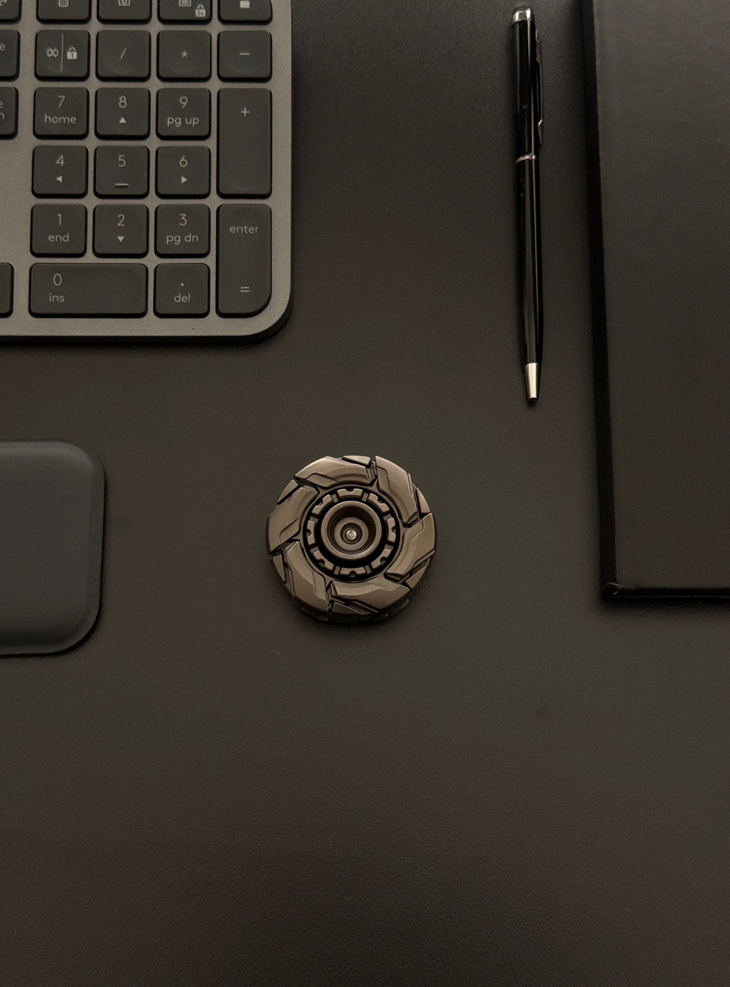 Robust metal fidget toy placed next to work accessories, emphasizing its premium and adult-oriented build
