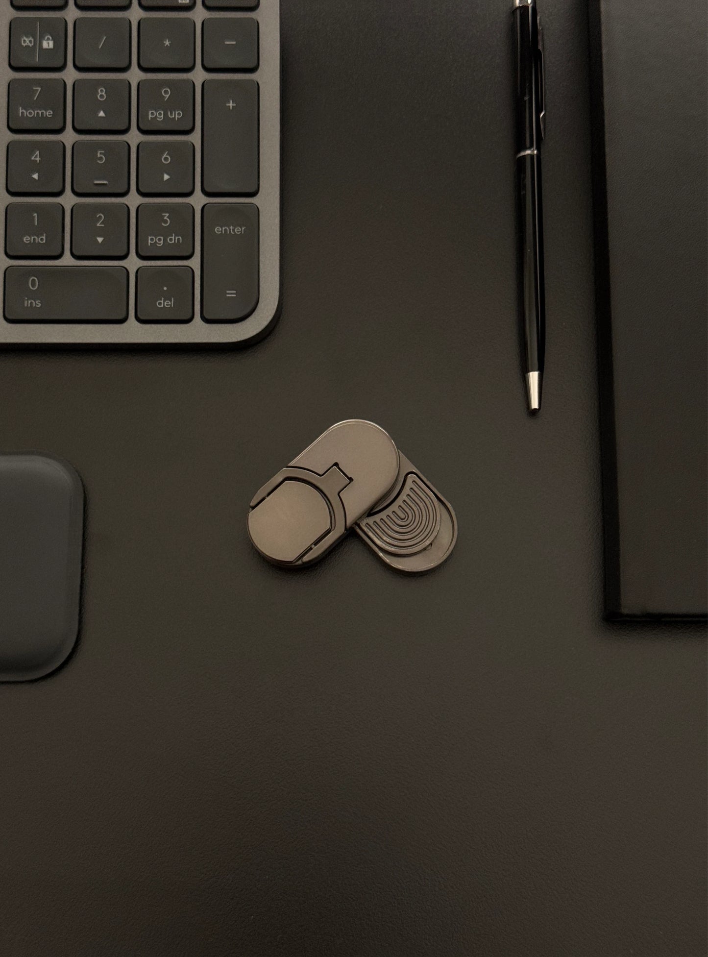 Coin slider fidget toy placed on a desk with a keyboard and notebook, emphasizing its suitability for work environments.​
