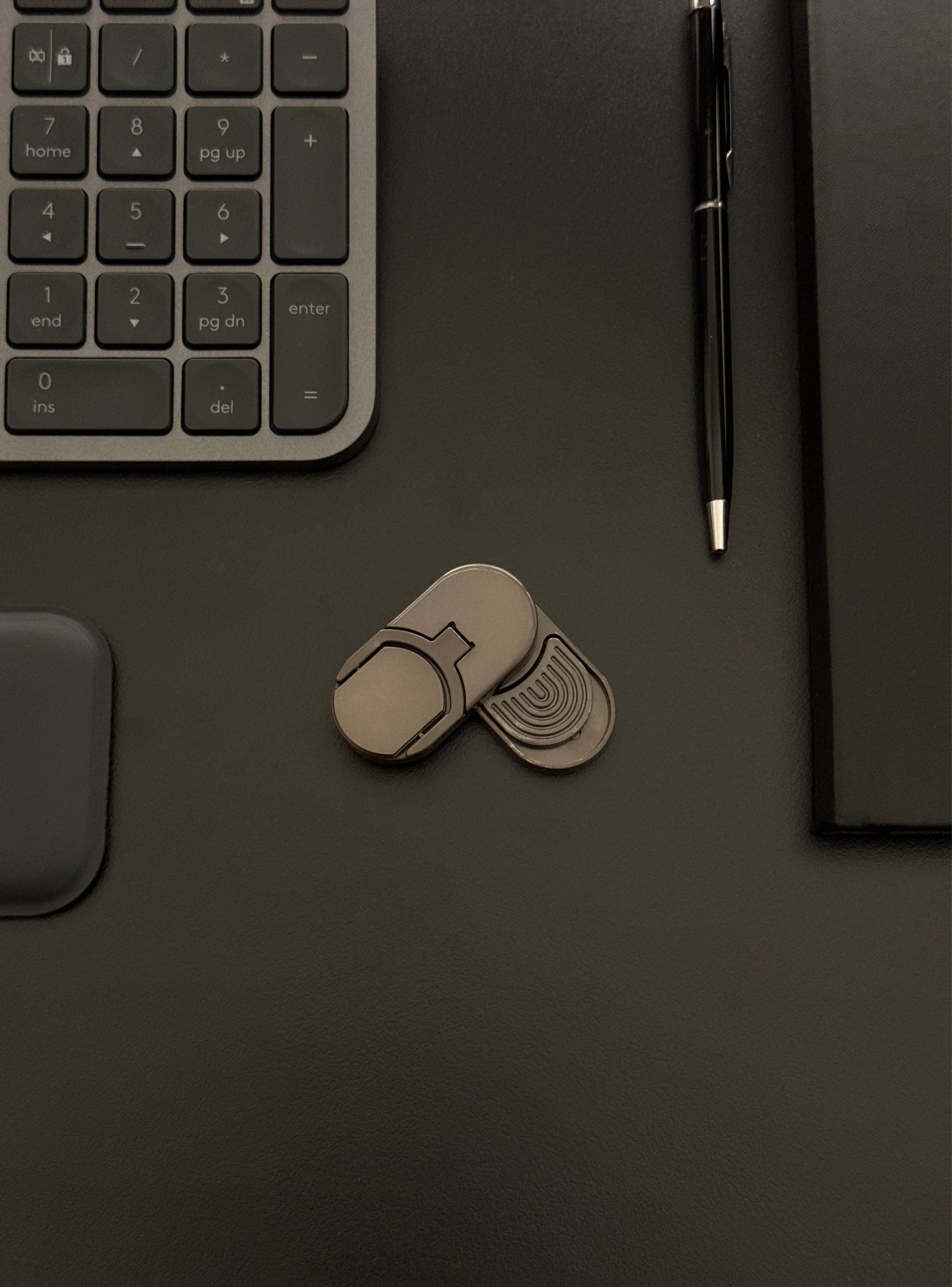Coin slider fidget toy placed on a desk with a keyboard and notebook, emphasizing its suitability for work environments.​

