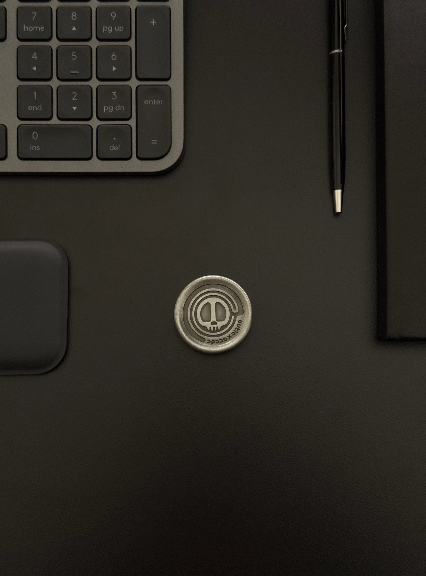 Skull Coin displayed on a desk setup featuring a keyboard and notebook, portraying its presence in a tech-savvy environment.
