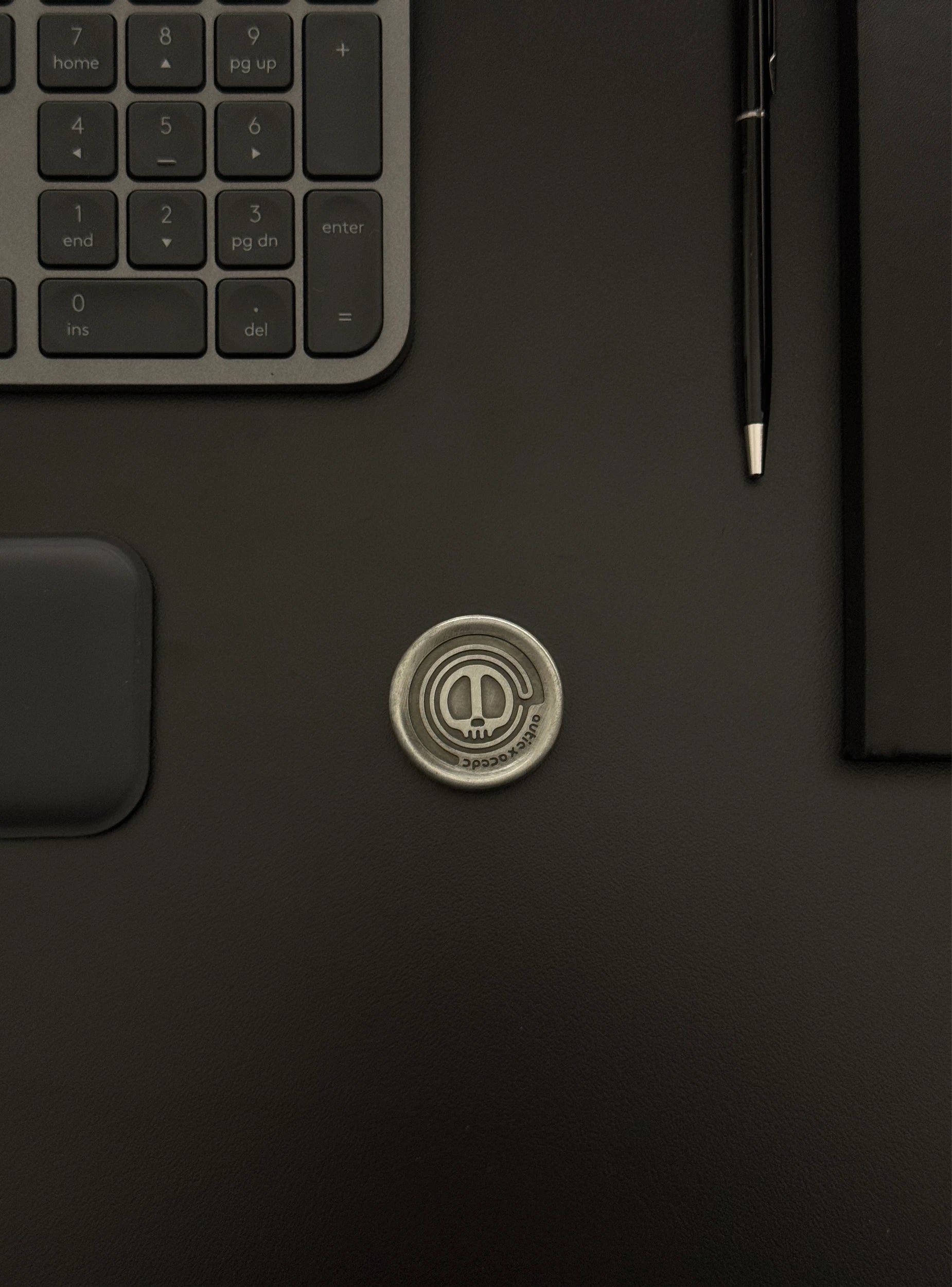 Skull Coin displayed on a desk setup featuring a keyboard and notebook, portraying its presence in a tech-savvy environment.
