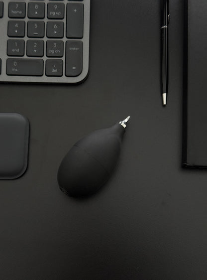Manual air blower resting on a work desk with keyboard and notebook, highlighting its aesthetic fit in tech setups